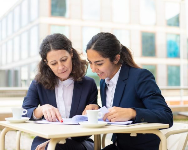 Businesswomen working with documents in outdoor cafe Businesswomen working with documents in outdoor cafe. Professional female colleagues in formal wear sitting at table, drinking coffee and discussing work in outdoor cafe. Coffee time concept